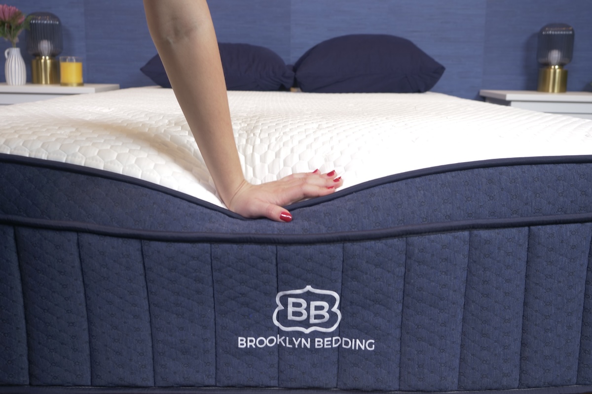 A woman’s hand presses down on the bottom edge of the Brooklyn Bedding Aurora Luxe Cooling. 