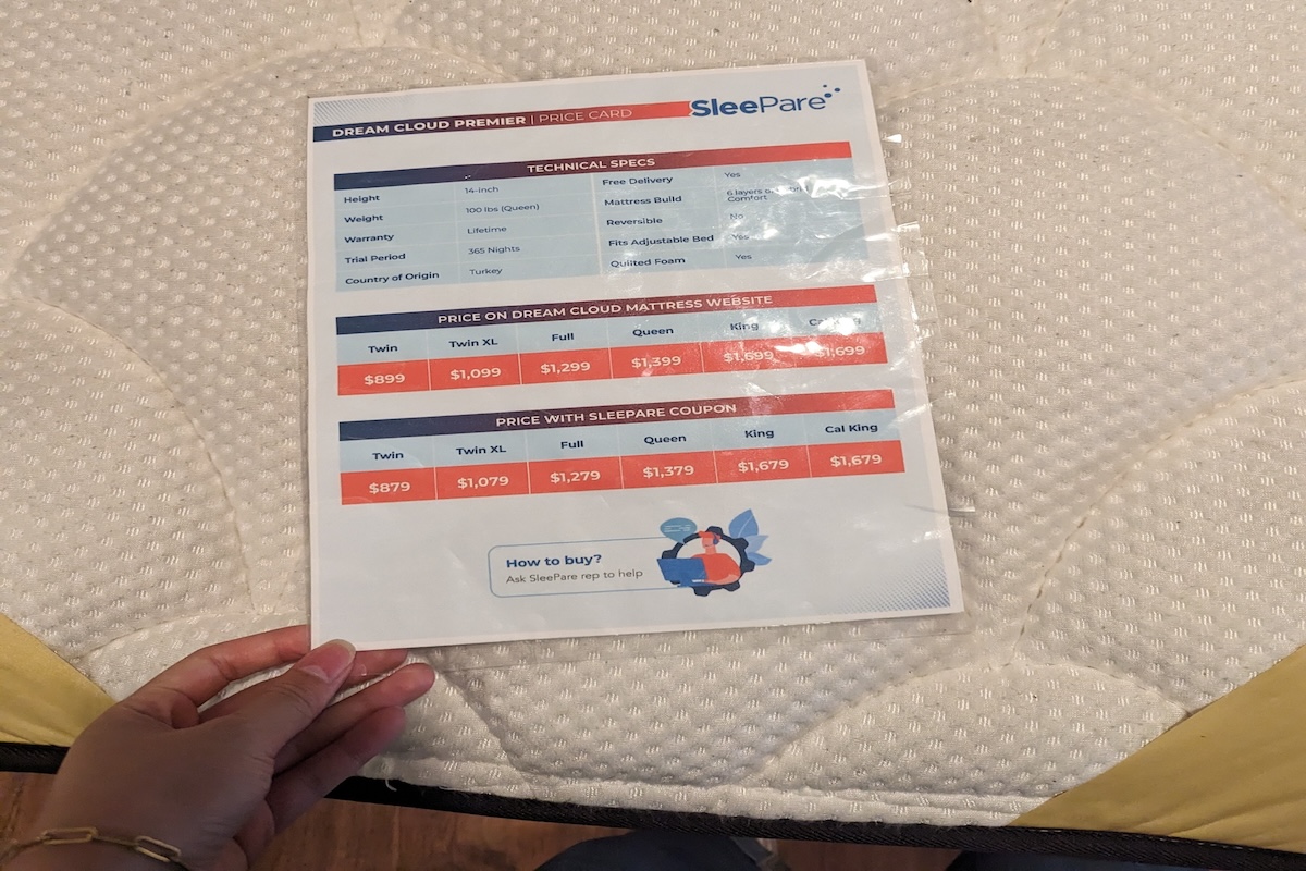 Woman’s hand holding the DreamCloud Premier price card over the mattress