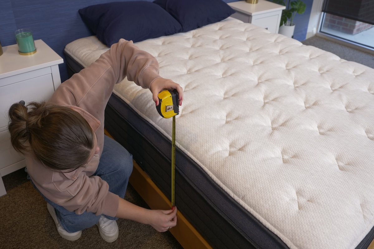 A woman uses a tape measure to measure the height of the Helix Midnight Luxe mattress.