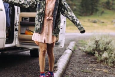 A woman in a pink dress and camouflage jacket balances on a log, showcasing the balance of skills needed to help an alcoholic loved one.