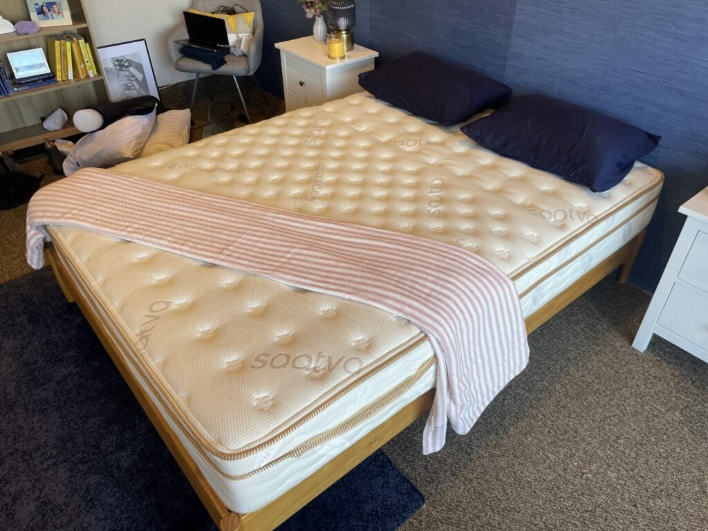 A Saatva Classic mattress viewed from above with navy pillows and a striped blanket