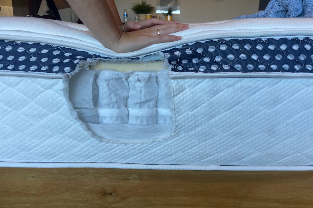 A woman pushes down on a mattress with a hole cut in the side to show the mattress’s interior construction